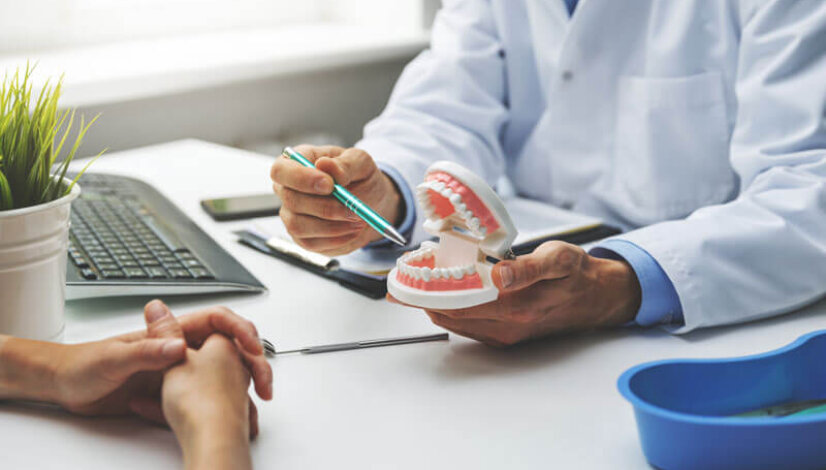 denturist sitting at a desk showing a model of teeth to a patient