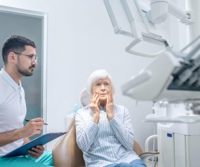 Senior Woman Holding Mouth in Pain at Denturist Office
