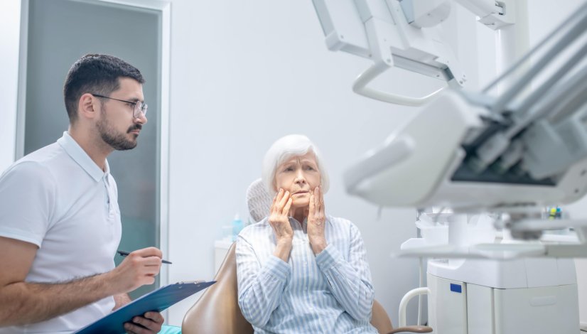 Senior Woman Holding Mouth in Pain at Denturist Office
