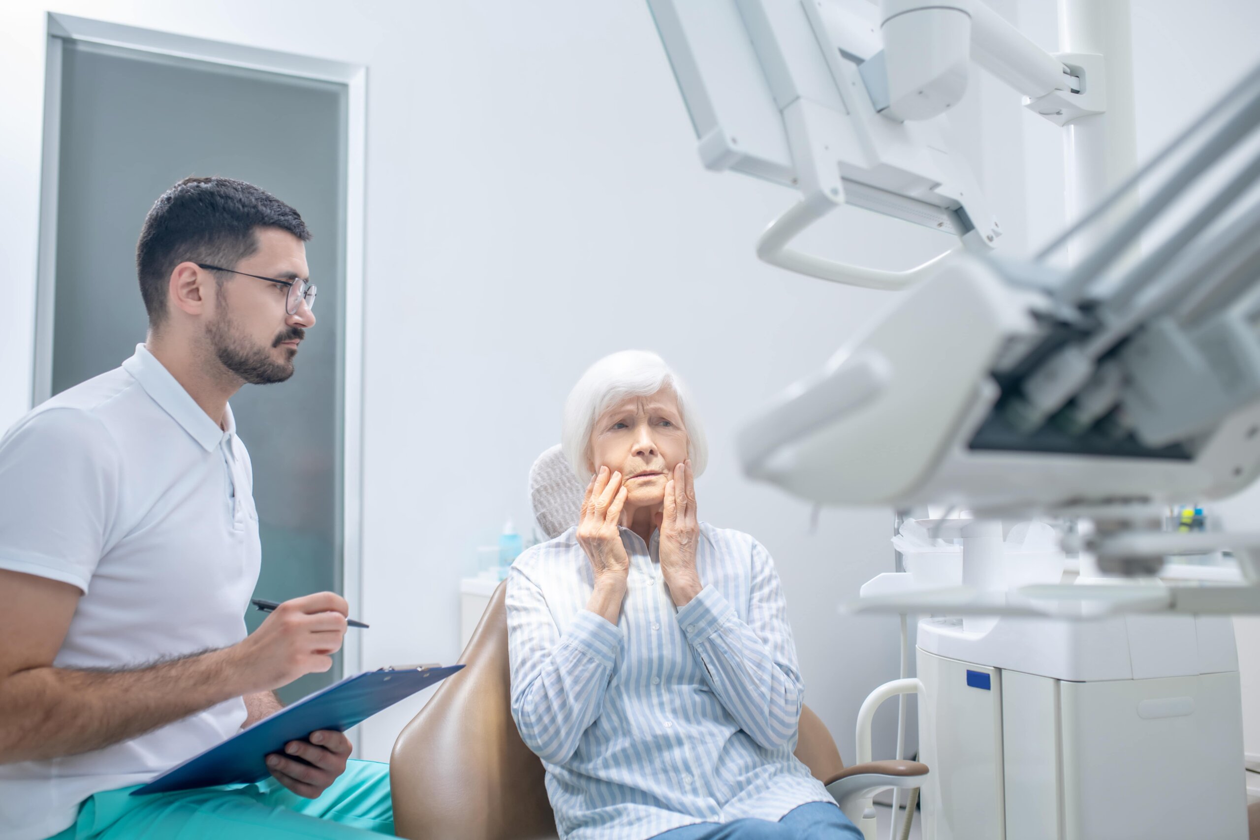 Senior Woman Holding Mouth in Pain at Denturist Senior Woman Holding Mouth in Pain at Denturist Office