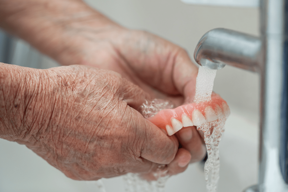 a person cleaning dentures under a faucet.
