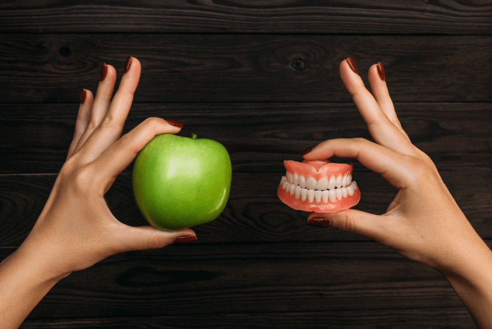 Person holding a set of denture in one hand and an apple in the other hand. 