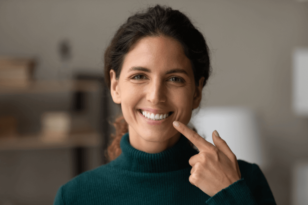 a young woman pointing at her smile. 