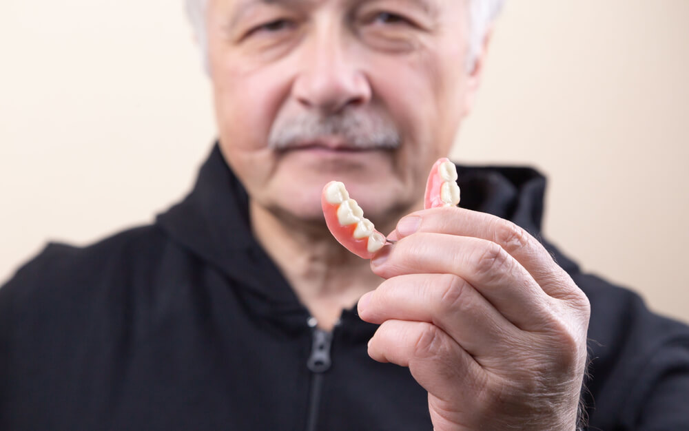 Gray-haired Man Holding Dentures - How Do Dentures Stay in Place